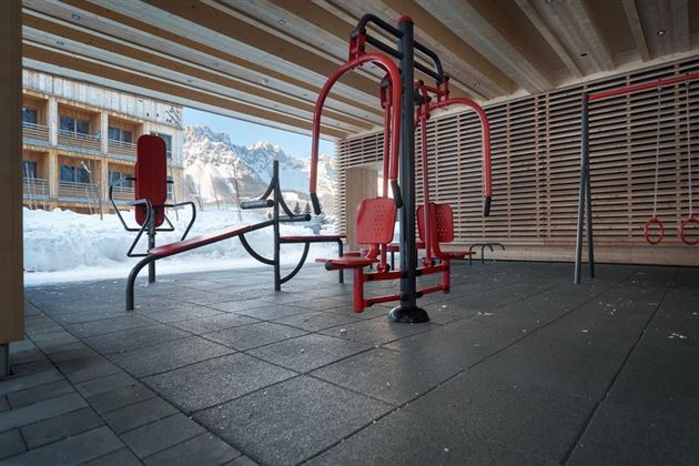 An outdoor fitness area with red equipment and a snow-covered environment. Snow-covered mountains are visible in the background.