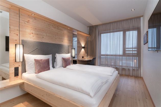 A modern bedroom with two single beds and wooden paneling. Large windows let in plenty of light and create a cozy atmosphere.
