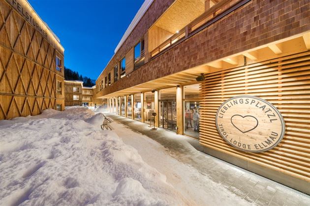 A modern lodge with wooden cladding and snow-covered ground. The clear evening sky gives the scene a cozy atmosphere.
