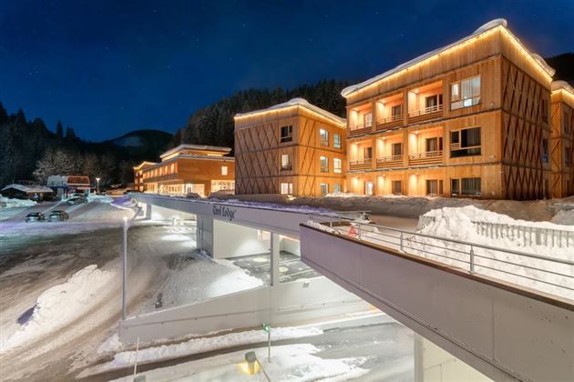 A modern building in the snow with warm light and a wooden facade. Surrounded by a tranquil winter landscape.