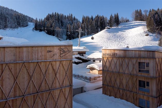 A winter mountain village with snow-covered hills and a cable car. Wooden buildings with traditional design complement the picturesque landscape.