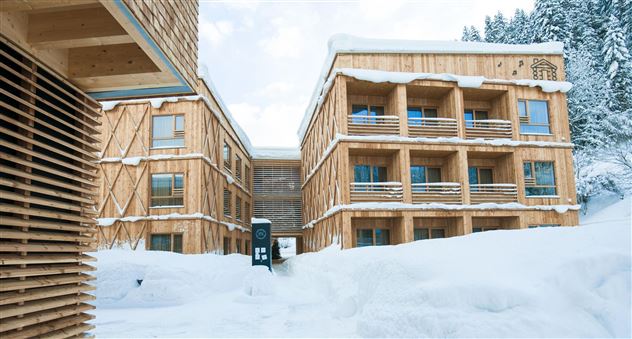 A modern wooden building in the snow, surrounded by a wintry landscape. The architecture is cozy and inviting, ideal for winter holidaymakers.