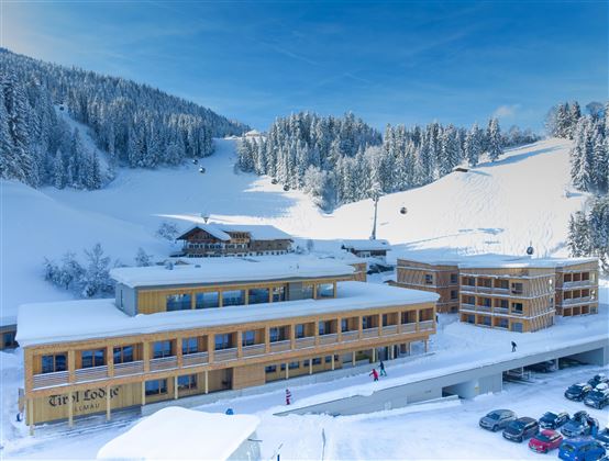 A modern hotel in a snowy landscape. In the background, there are snow-covered mountains and skiing activities visible.