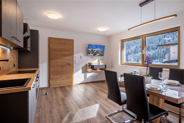 Een moderne keuken met een eetgedeelte en grote ramen die uitzicht op de bergen bieden. De ruimte is licht en uitnodigend, met houten meubels en stijlvolle details.