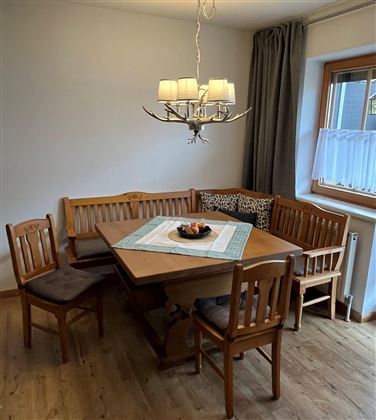A cozy dining area with a wooden table and benches. A modern lamp hangs from the ceiling, and a window provides plenty of light.