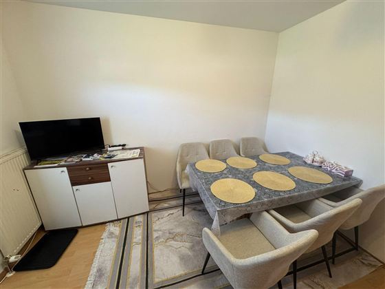 A modern dining area with an elegant table and chairs. In the background, there is a television and a sideboard.