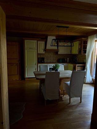A cozy kitchen with a wooden table and modern chairs. The decor is bright and inviting, with large windows that let in daylight.