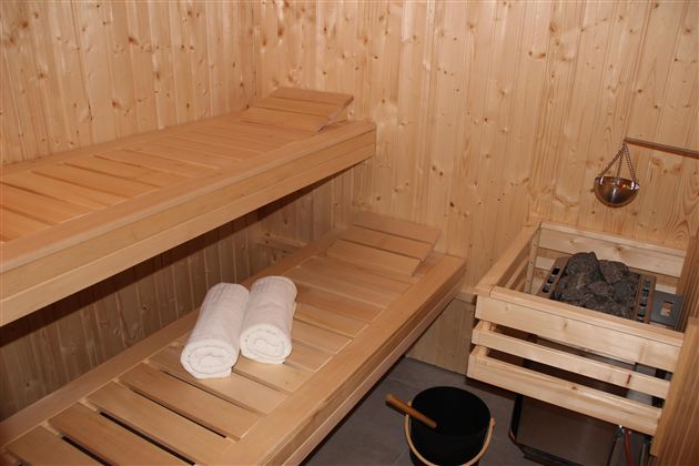 Eine gemütliche Sauna aus Holz mit zwei Bänken und sauberen Handtüchern. Neben der Saunabank befinden sich ein Saunaofen und ein Eimer.
