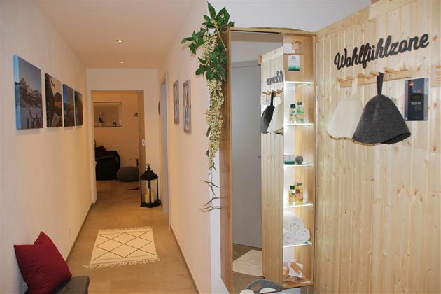 Ein einladender Flur mit natürlichen Holzelementen und einem Bereich für Wohlfühlprodukte. Gemütliche Dekoration und sanftes Licht schaffen eine entspannende Atmosphäre.