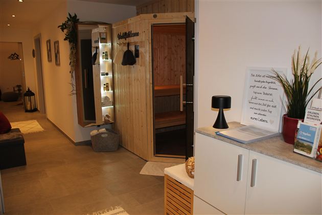 Ein gemütlicher Empfangsbereich mit einer Holzsauna. Auf der linken Seite stehen Pflanzen und ein Tisch mit Dekoration.