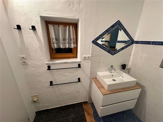 Ein modernes Badezimmer mit einem Waschbecken und einem drehbaren Spiegel. Im Hintergrund sind ein Fenster und Handtuchhalter zu sehen.
