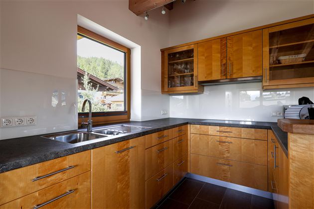 Eine moderne Küche mit Holzschränken und einer großen Fensteransicht. Die Arbeitsfläche ist aus schwarzem Material und bietet viel Platz zum Kochen.