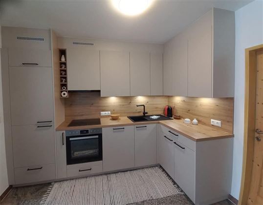 A modern kitchen with light furniture and wooden details. The equipment includes a stove, an oven, and an elegant sink.
