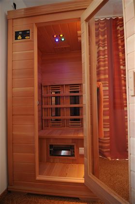 A sauna with wooden paneling and colorful lights. It is located in a room with a curtain and a mirror.