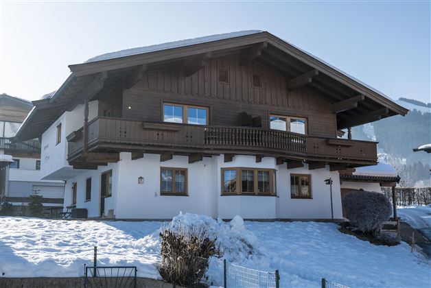 A charming wooden house in alpine style, surrounded by snow. The mountains are visible in the background, and the sky is clear.