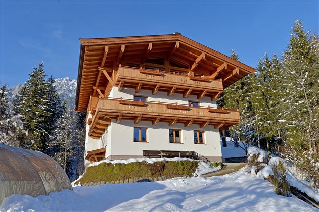 Ein schönes Chalet im Schnee umgeben von Bäumen. Der blaue Himmel sorgt für eine malerische Winteratmosphäre.
