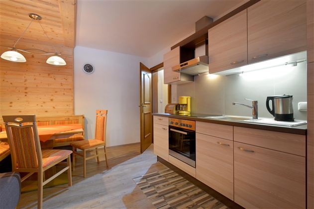 A modern kitchen with wooden cabinets and a dining area. The equipment includes a stove, a kettle, and a quiet atmosphere.