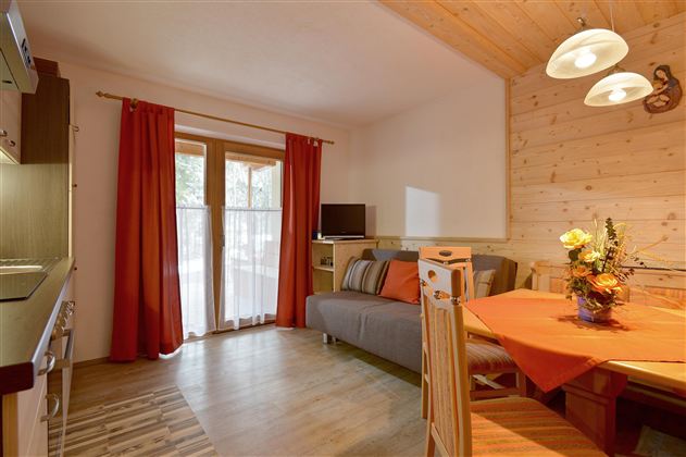 A cozy living space with a sofa, dining table, and a modern kitchenette. The red curtains and wooden paneling create a warm atmosphere.