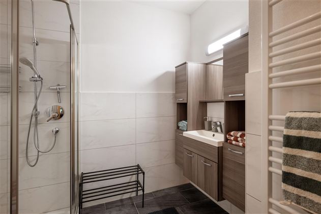 A modern bathroom with a shower and wooden cabinets. The walls are brightly tiled and a towel rack is located on the wall.