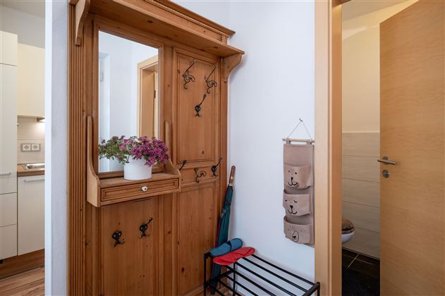 An inviting hallway with a wooden cabinet and a small mirror. Next to the cabinet are colorful umbrellas and a decorative storage holder.