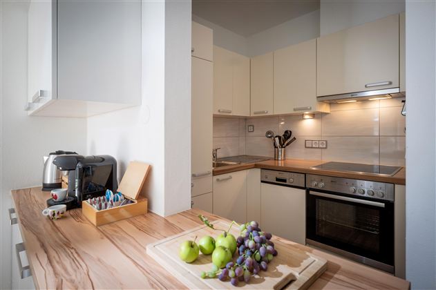 A modern kitchen with bright cabinets and a wooden countertop. On the table are green apples and grapes.