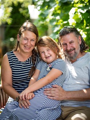 A happy family sits in the garden. The mother, the father, and the child are smiling happily at the camera.