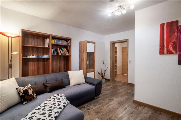 A cozy living room with a gray sofa and shelves. The room has warm lighting and wood tones that create an inviting atmosphere.