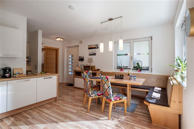 A modern kitchen with a dining table and colorful chairs. Plenty of light flows through the windows, and the wood design creates an inviting atmosphere.