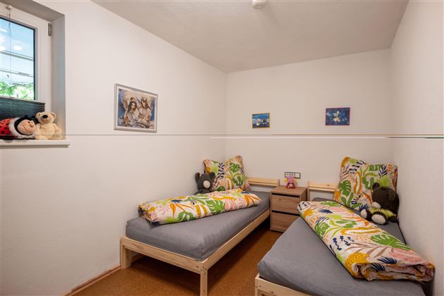 A simple bedroom with two beds and colorful bedding. There are some pictures on the wall and a small nightstand between the beds.