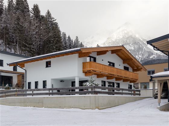 Ein modernes Haus in einer schneebedeckten Landschaft. Im Hintergrund sind Berge und Bäume zu sehen.