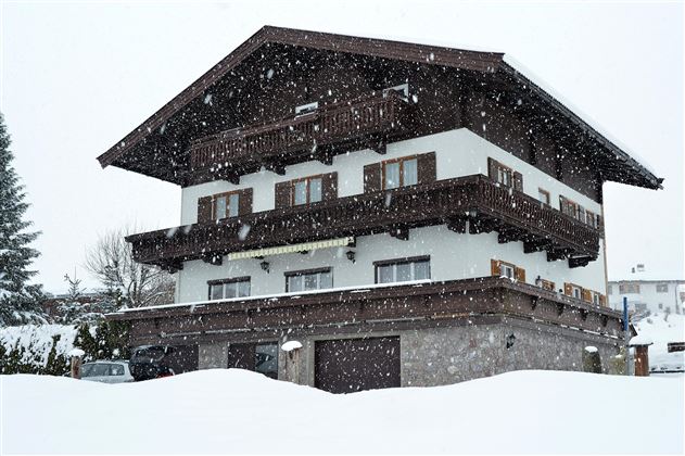 Een charmant huis in de sneeuw met meerdere balkons. De sneeuw valt zachtjes en bedekt het landschap.