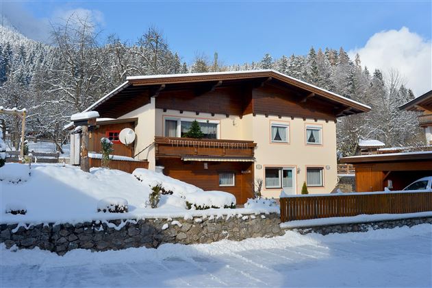 Ein charmantes Haus im Schnee, umgeben von verschneiten Bäumen. Die Landschaft erinnert an eine idyllische Winterlandschaft.