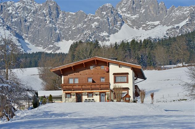 A charming house amidst a snow-covered landscape. Majestic mountains rise in the background.