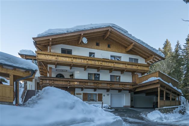 Ein charmantes Gebäude im alpinen Stil, umgeben von Schnee. Die Holzbalkone und die Gestaltung verleihen dem Haus eine gemütliche Atmosphäre.