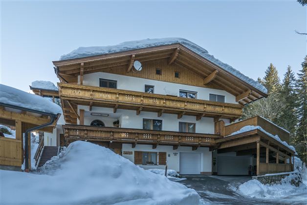 A charming building in alpine style, surrounded by snow. The wooden balconies and the design give the house a cozy atmosphere.