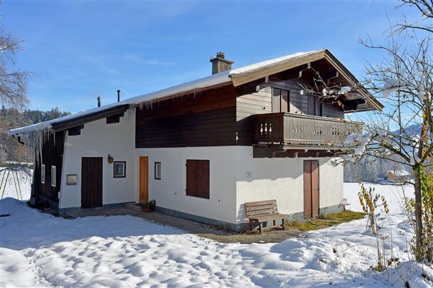 Ein traditionelles Haus im Alpenstil, umgeben von Schnee. Der klare blaue Himmel sorgt für eine ruhige Winteratmosphäre.
