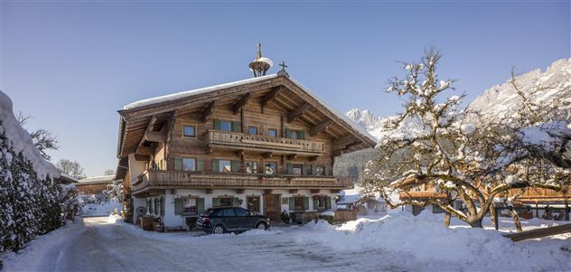 Ein rustikales Holzhaus im Winter, umgeben von Schnee. Der Himmel ist klar und die Landschaft wirkt friedlich.