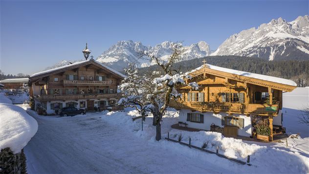 Ein winterliches Panorama mit schneebedeckten Bergen. Zwei gemütliche Holzhäuser stehen in einer ruhigen Landschaft.
