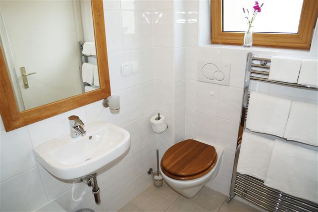 Ein modernes Badezimmer mit einer weißen Wandfliesen und einem Holzboden. Es verfügt über ein Waschbecken, eine Toilette und frische Handtücher.