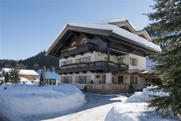 Ein charmantes Chalet im Winter mit schneebedecktem Grundstück. Die sonnigen Fenster und Balkone verleihen dem Gebäude einen einladenden Charakter.