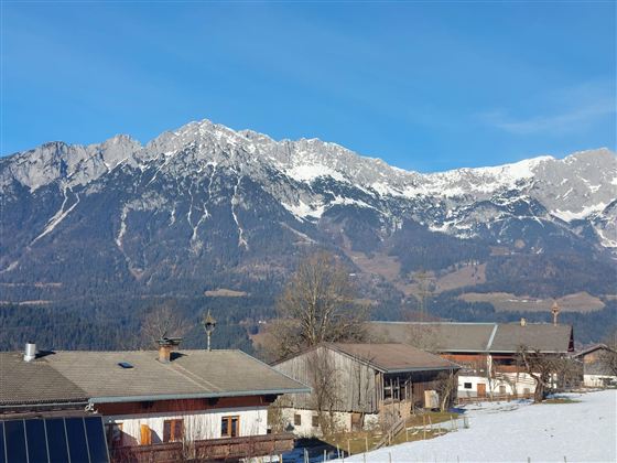 Eine majestätische Berglandschaft mit schneebedeckten Gipfeln und klarem blauem Himmel. In der Vordergrund sind traditionelle, alpine Häuser zu sehen.