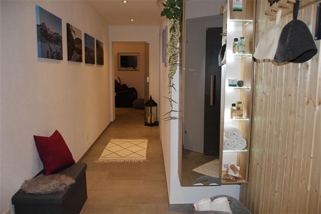 Ein heller Flur mit modernen Dekorationen und einem großen Spiegel. Auf der linken Seite sind Bilder an der Wand und ein gemütlicher Sitzbereich.