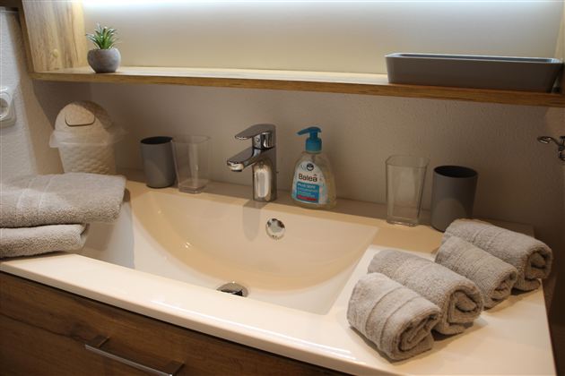 Ein modernes Badezimmer mit einem Waschbecken und Handtüchern. Auf dem Waschbecken stehen Seife und Gläser.