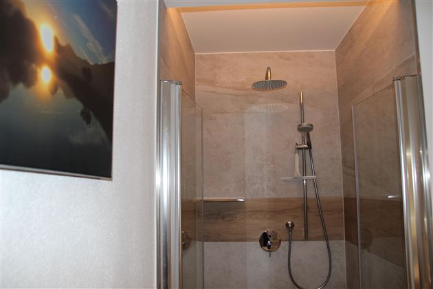 Eine moderne Duschkabine mit transparenten Wänden und einer schlichten Dusche. Im Hintergrund ist ein Bild mit einem Sonnenuntergang zu sehen.