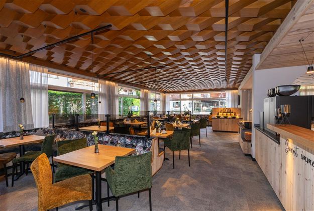 A modern restaurant with bright wooden paneling and comfortable seating. Large windows let in plenty of light and offer a view of the outdoor areas.