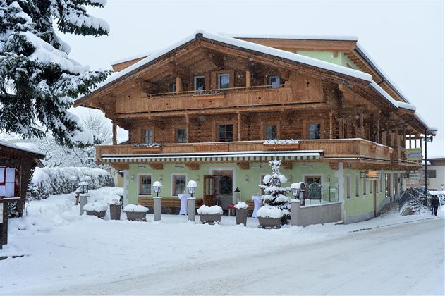 Ein gemütliches Holzhaus im Schnee. Die Umgebung ist winterlich und ruhig, mit einer schneebedeckten Straße.