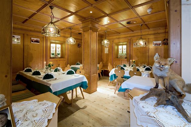 Ein rustikales Restaurant mit Holzwänden und liebevoll dekorierten Tischen. Ein Fuchs steht auf einem Regal und verleiht dem Raum eine besondere Atmosphäre.