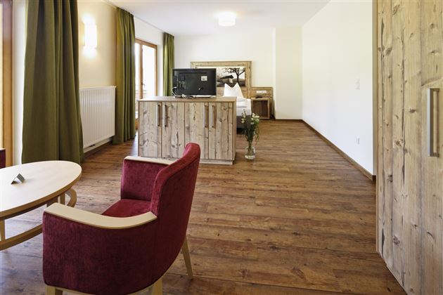 Ein modernes Zimmer mit Holzboden und großen Fenstern. Es gibt einen roten Stuhl, einen Tisch und einen Fernseher auf einer Holzkommode.