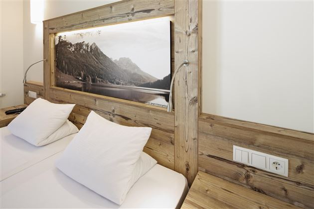 Ein elegantes Schlafzimmer mit zwei Betten und weißen Kissen. Im Hintergrund ist ein Bild von einer Berglandschaft zu sehen.