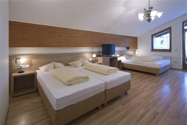 Ein gemütliches Hotelzimmer mit zwei Einzelbetten und einem Doppelbett. Die Einrichtung ist modern und hell, mit Holzpanelen und einem großen Fenster.